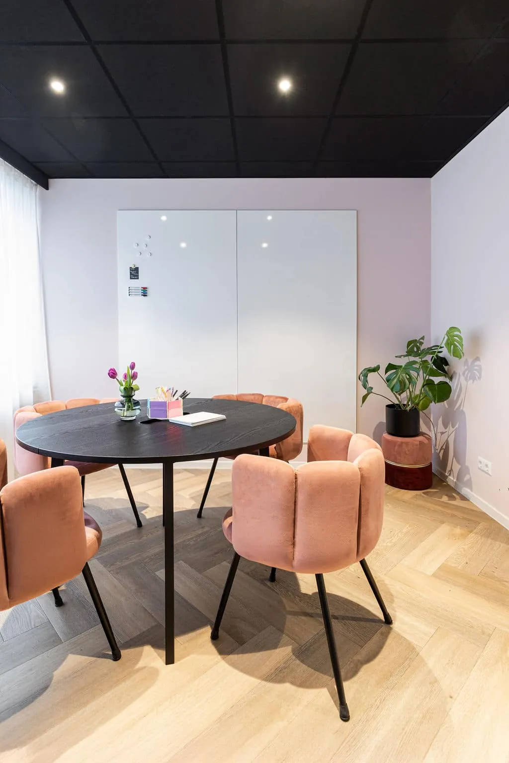 Een ronde tafel met roze fluwelen stoelen in een lichte vergaderruimte met planten