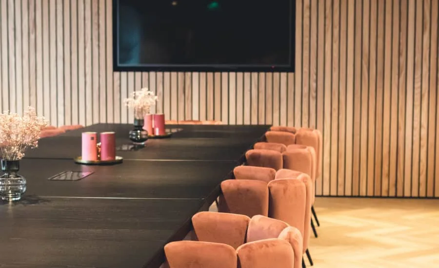 Een langgerekte vergaderruimte met houten lamellen aan de wand en roze stoelen