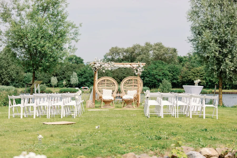 Het trouweiland met witte stoelen en een bloemenboog aan het water