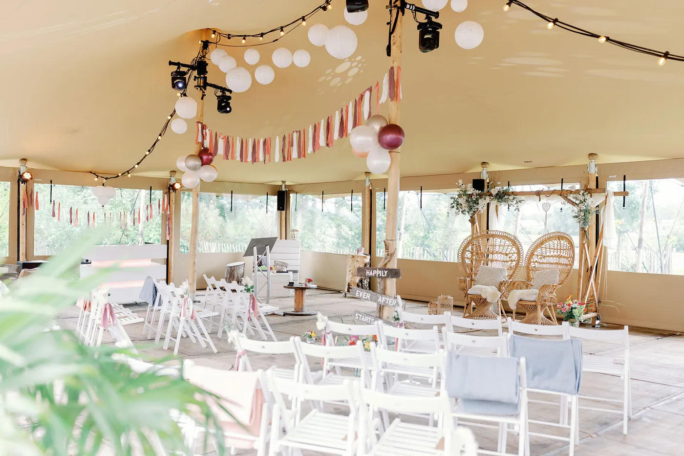 De feesttent van binnen met witte stoelen, lampionnen en slingers