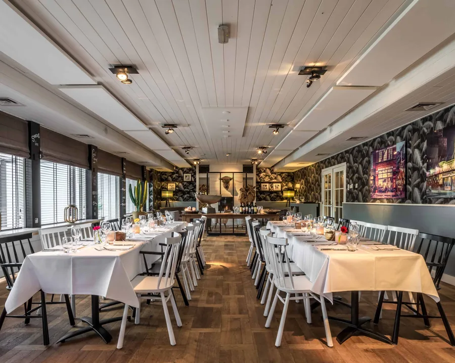 Een zaal met lange, wit gedekte tafels, witte stoelen en botanisch behang