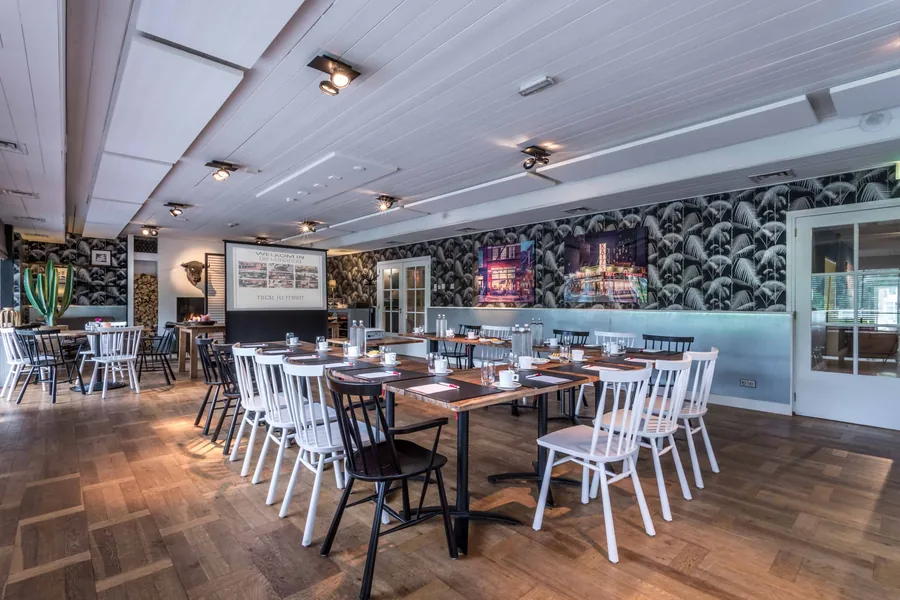 The Living met houten tafels en witte stoelen, klaar voor een vergadering