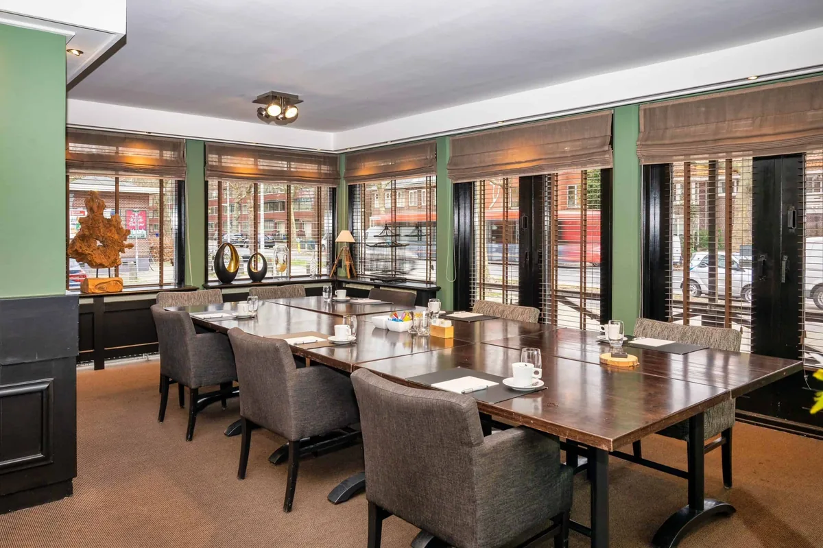 Een vergaderopstelling met grijze stoelen rond een lange tafel bij de ramen