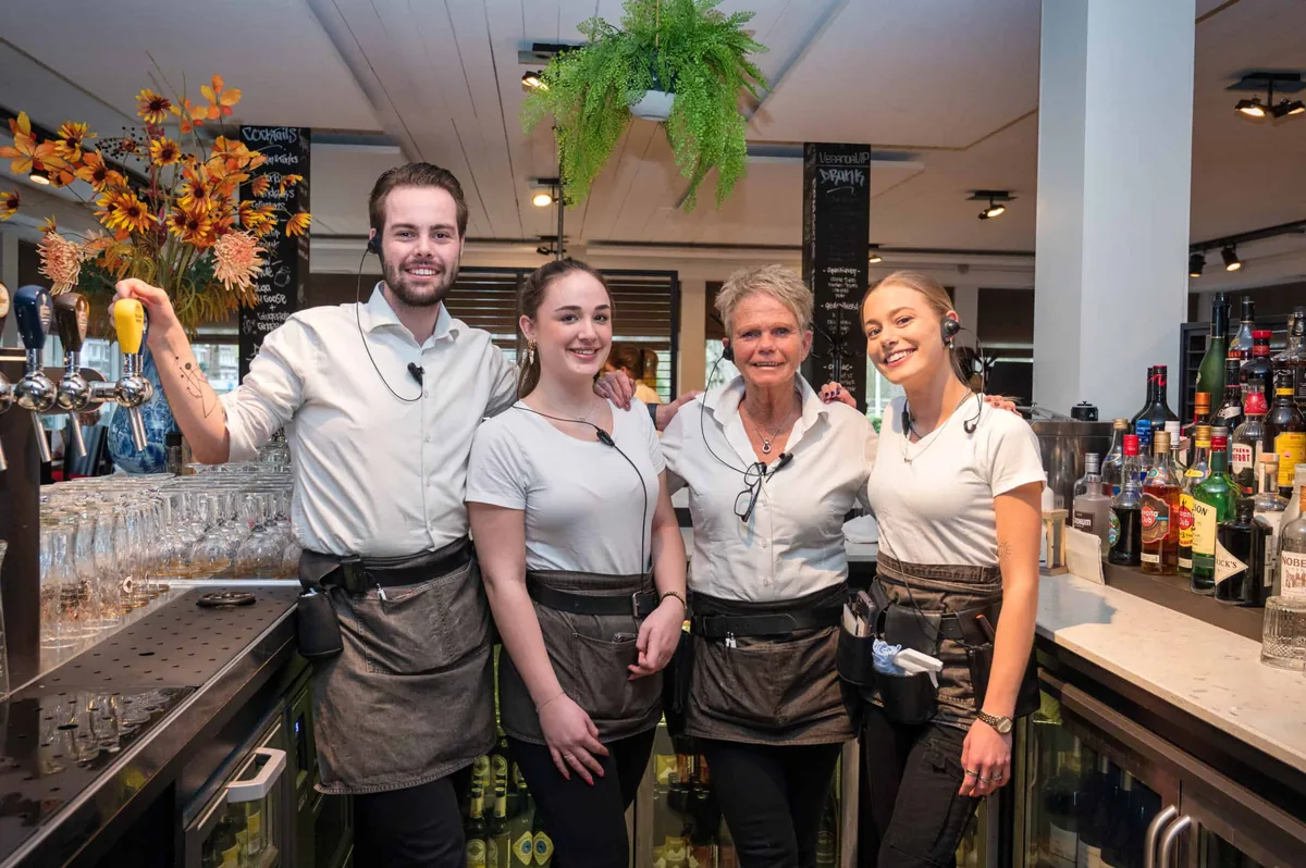 Vier medewerkers van De Veranda staan lachend achter de bar