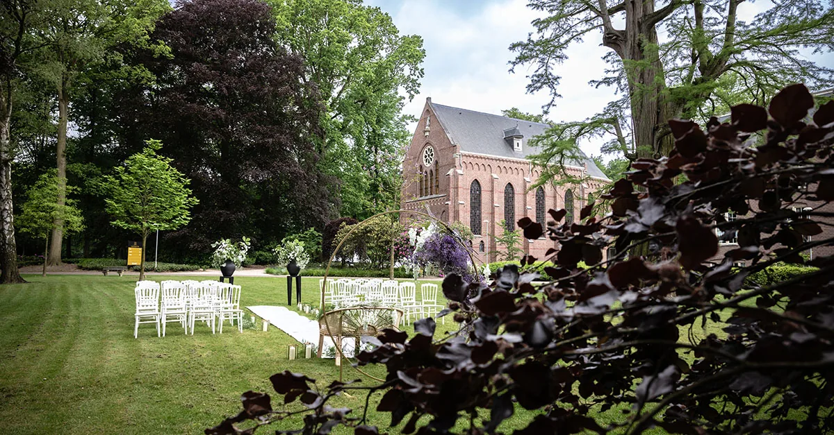 Rijen witte stoelen in de tuin van Kasteel Bijstervelt, met de kapel erachter