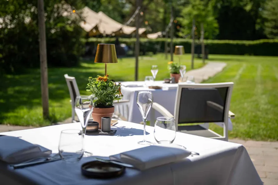 Een gedekte tafel op het terras in de tuin, met een tent op het gazon erachter