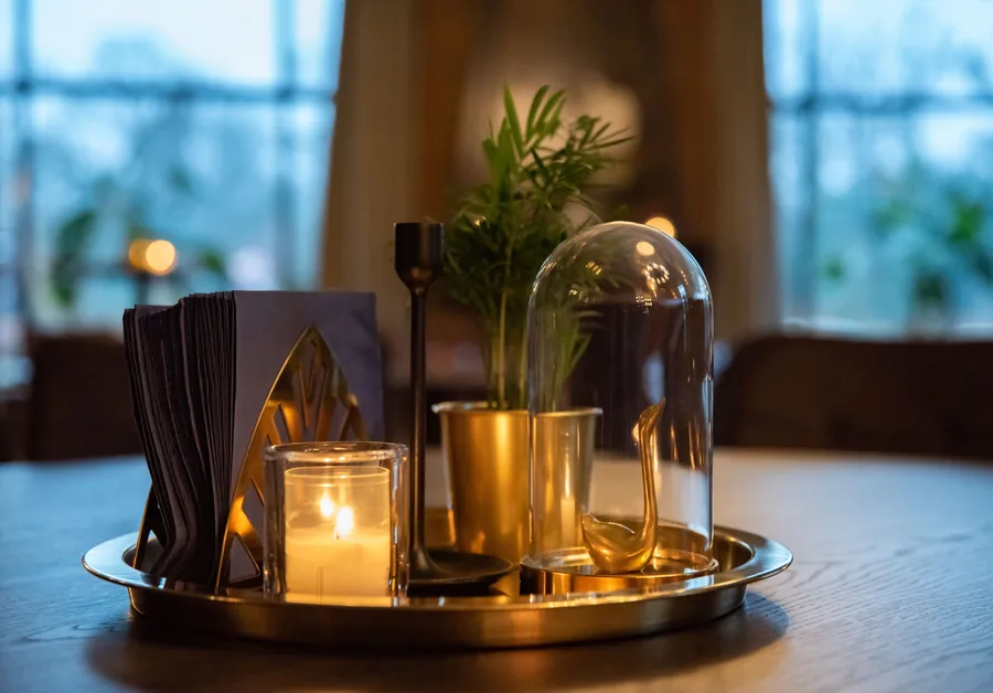 Een gouden dienblad met kaarsen, een plantje en een stolp op een tafel in het restaurant