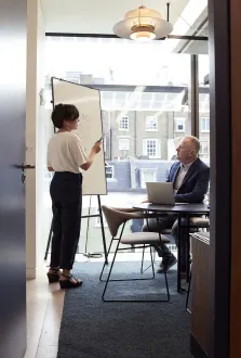 Een training op locatie: uitleg aan een flip-over, met een deelnemer achter zijn laptop